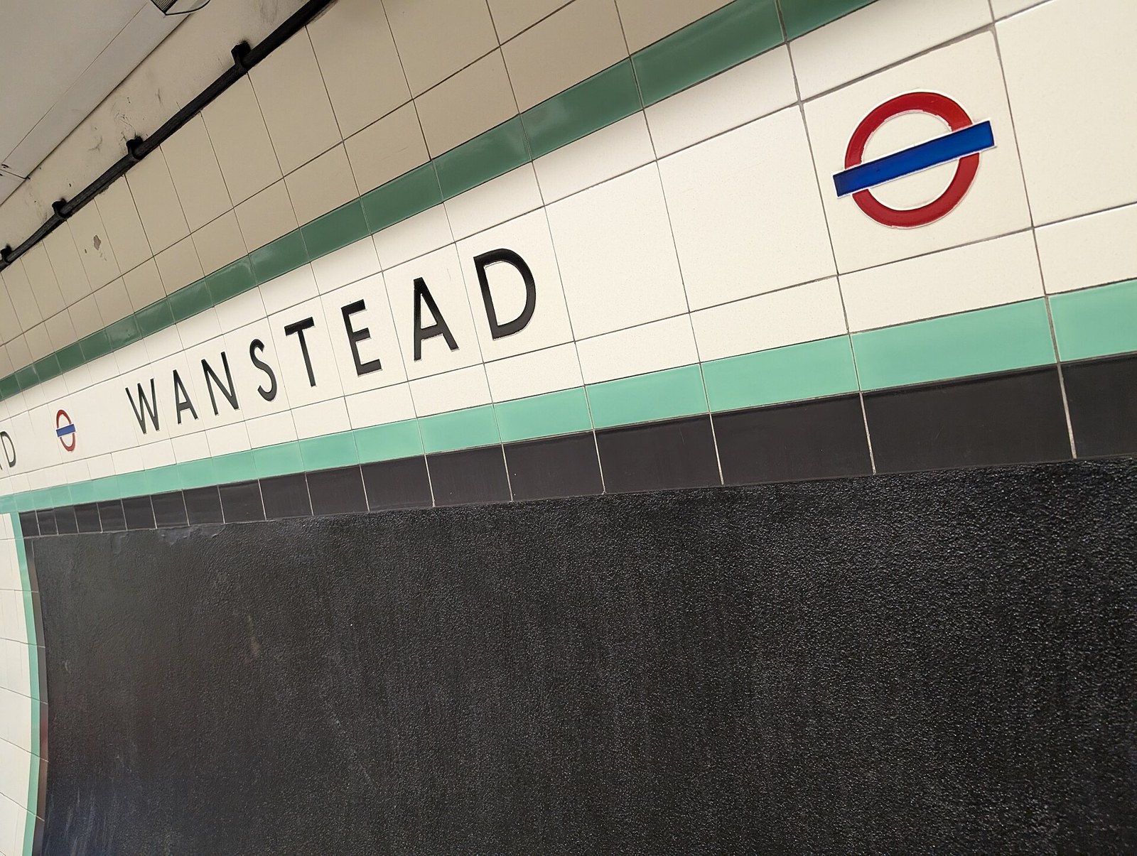 Green and cream wall tiles with the station name Wanstead and a London Underground roundel