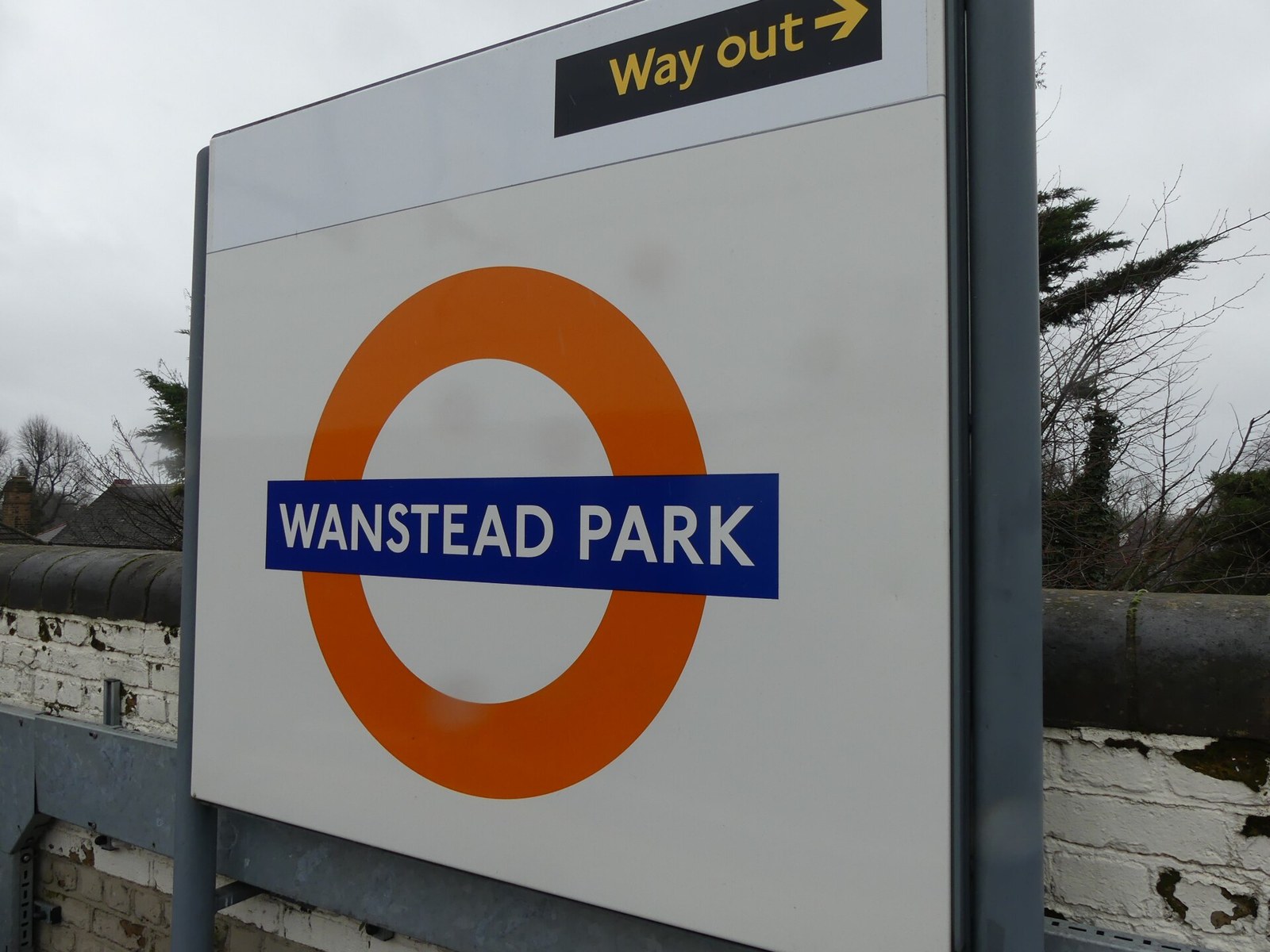 A white Overground station sign with an orange roundel reading Wanstead Park