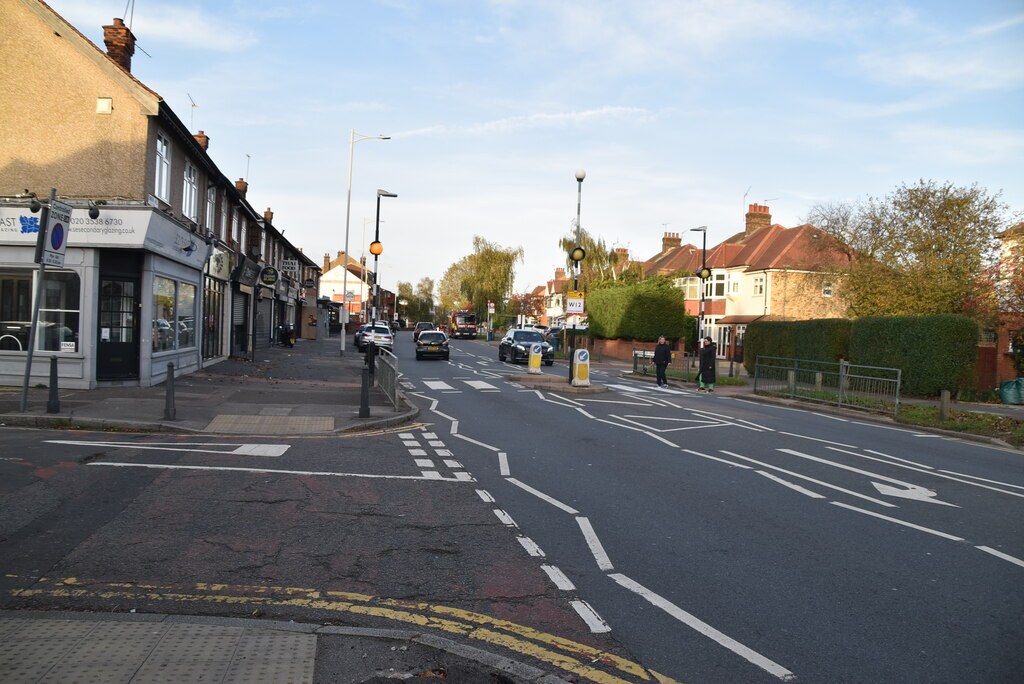 A row of shops on the left of Hermon Hill at a junction, with traffic lights, a crossing and a red fire engine in the distance