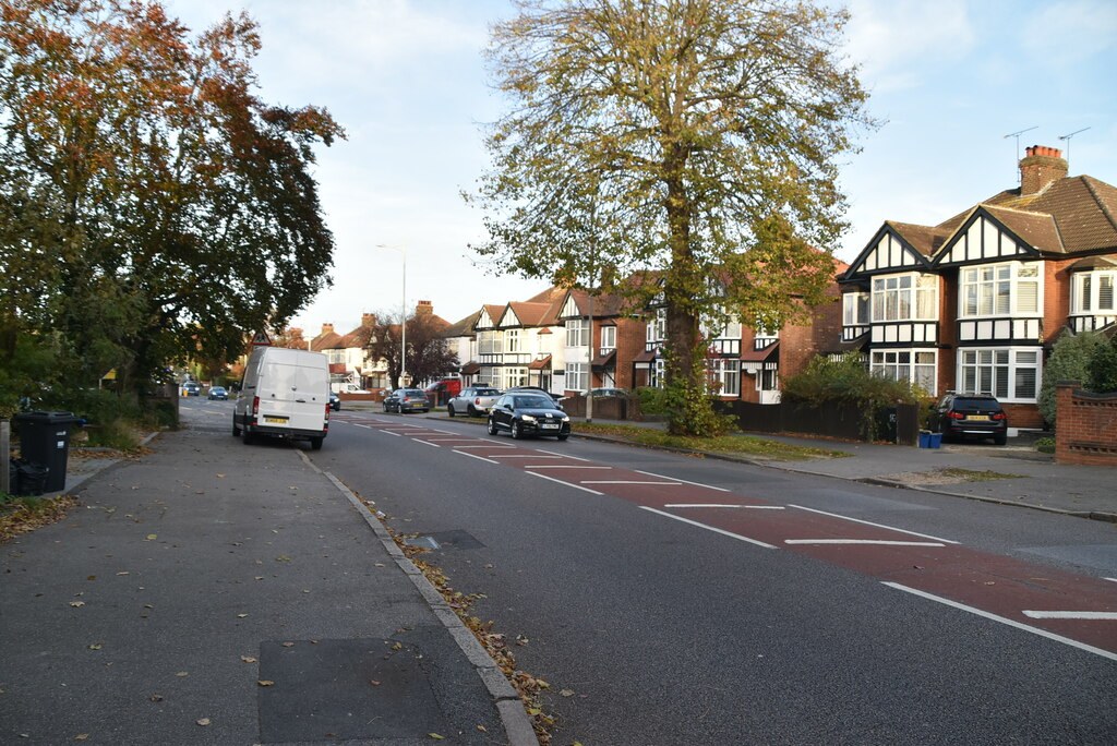 Mock-Tudor semi-detached houses on the right of a wide road with a red-surfaced bus lane marking and parked cars